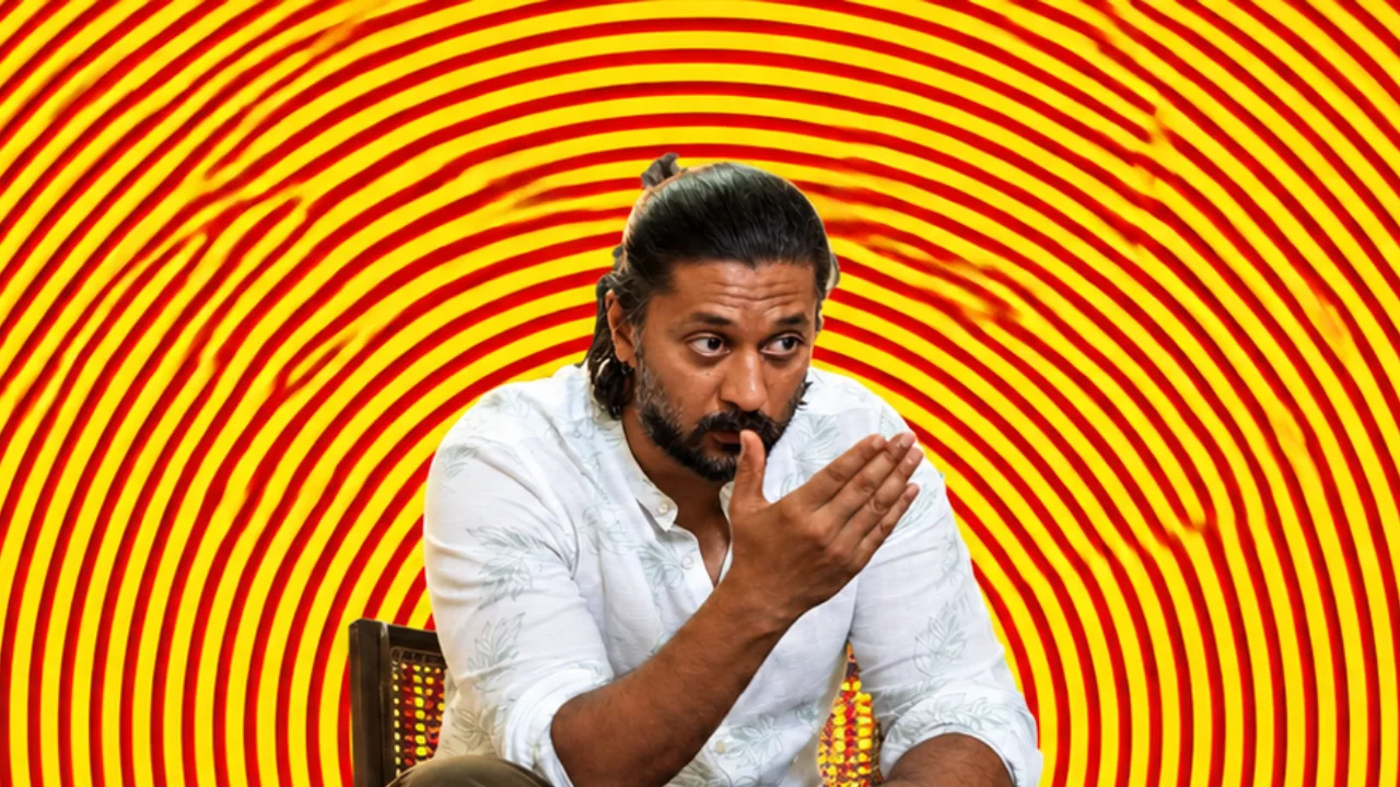 Chetan Ahimsa seated and gesturing mid-conversation, against concentric red and yellow rings